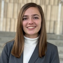 Jenna Springer is shown in front of a neutral background wearing a white turtleneck under a grey blazer
