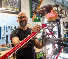 Nikka Singh smiles as he works on a red bike in a neatly organized bike shop.