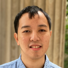 A close-up of Timothy Yen wearing a blue-collared shirt on a beige background.