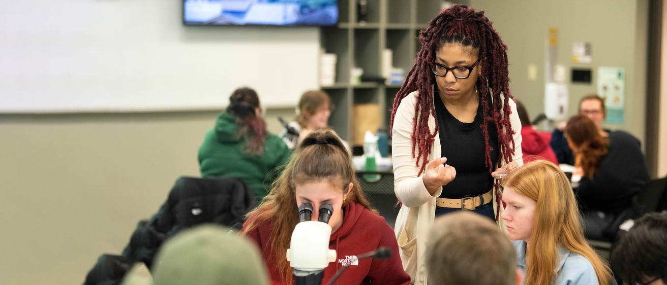 Instructor watching students look into a microscope 
